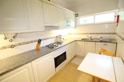 a white kitchen with white cabinets and a table at Apt T2 Jardins do Castelo - Albufeira, Algarve in Albufeira