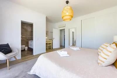 a white bedroom with a bed and a chair at Villa Casinha in Albufeira