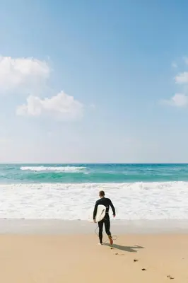 a man walking on the beach with a surfboard at Vila Portuguesa by MTPhomes in Albufeira