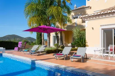 a villa with a swimming pool with chairs and a purple umbrella at Casa da Colina in Loulé