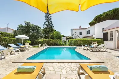 a swimming pool with tables and umbrellas next to a house at A Fantastic Place for Families, Hilton Hotel are and close to amenities in Quarteira