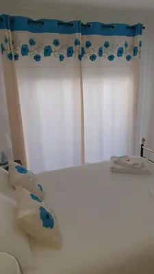 a bedroom with a white bed with a blue curtain at Quarteira Beach in Quarteira