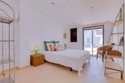 a white bedroom with a bed and a chair at Casa Luz - Quarteira in Quarteira