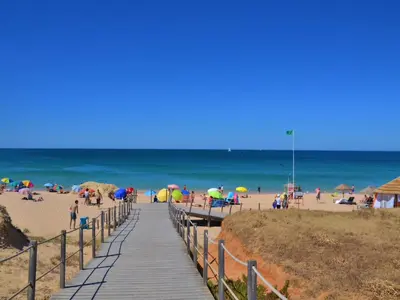 a wooden boardwalk leading to a beach with people with umbrellas at Luxury Apartment, 3 min Walk to Beach, Albufeira in Guia