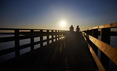 two people walking on a pier at sunset at Apartamentos Vila das Lagoas – Salgados in Guia