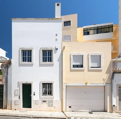 a white house with a green door and a garage at Downtown Pool House in Faro