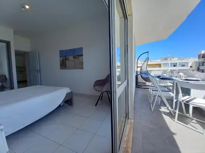 a bedroom with a bed and a table on a balcony at T2 Gaveto- Frente Mar, Wifi, Aconchegante & Familiar in Quarteira