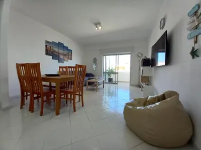 a dining room and living room with a table and chairs at T2 Gaveto- Frente Mar, Wifi, Aconchegante & Familiar in Quarteira