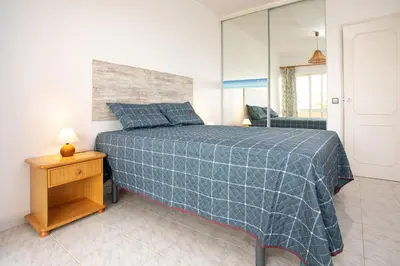 a bedroom with a bed with a blue blanket and a mirror at O Apartamento A Ramos Palmeira Galé Está inserido num Condomínio com PISCINA, Fica apenas a 250 Metros da Praia da Galé - Apartamento com Ar Condicionado na Sala, Smart TV com Prime Vídeo e Cozinha Completa in Albufeira