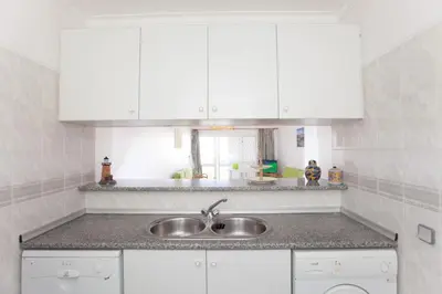a kitchen with a sink and white cabinets at O Apartamento A Ramos Palmeira Galé Está inserido num Condomínio com PISCINA, Fica apenas a 250 Metros da Praia da Galé - Apartamento com Ar Condicionado na Sala, Smart TV com Prime Vídeo e Cozinha Completa in Albufeira