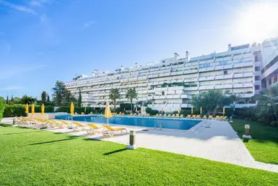 a large building with a swimming pool with chairs and a building at Apartamento dentro da Marina de Vilamoura in Vilamoura