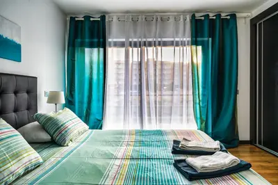 a bedroom with a bed with blue curtains and a window at Townhouse 3 Bedroom Townhouse Olhos de Agua Communal pool AT03 in Olhos de Água