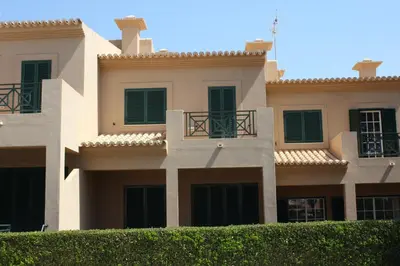 a building with green shuttered windows and a hedge at Villa V2 X in Albufeira