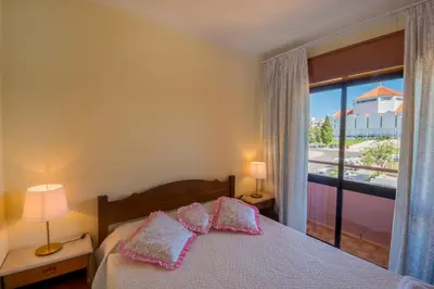 a bedroom with a bed with pink pillows and a window at Apartamento São Pedro do Mar in Quarteira