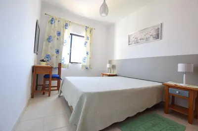a white bedroom with a bed and a window at Apartamentos Carruna in Albufeira