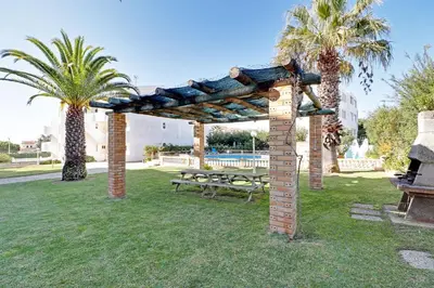 a wooden pergola with a picnic table and palm trees at Albufeira Delight with Pool by Homing in Guia