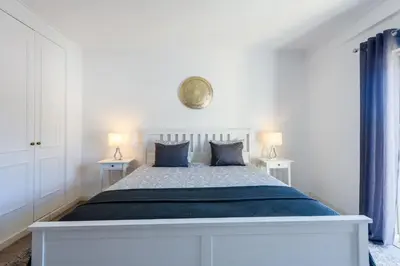 a white bedroom with a large bed with blue pillows at Amazing apartment in Albufeira in Albufeira