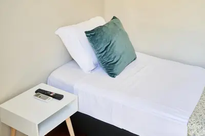 a white bed with a green pillow and a side table at Baron Faro - Guest House in Faro