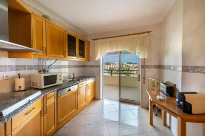 a kitchen with wooden cabinets and a table with a microwave at AL - Maré in Albufeira