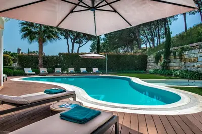 a swimming pool with chairs and an umbrella at Villa Mayfair - Quinta do Lago in Almancil