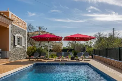 a swimming pool with two red umbrellas and chairs and a pool at Laura by Algarve Villa Holidays in Albufeira