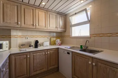 a kitchen with wooden cabinets and a sink and a window at Hopstays Vilamoura All In - Marina View Apartment in Vilamoura