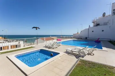 a swimming pool with chairs and the ocean in the background at Apartamento sobre a praia in Olhos de Água
