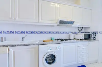 a white kitchen with a washing machine and a sink at Mango Apartment - Faro city center in Faro