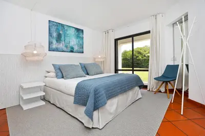 a white bedroom with a bed and a blue chair at Albufeira Club 98 - O refúgio perfeito in Albufeira