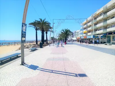 a sidewalk on a beach with palm trees and buildings at Varandas do Mar 3- Remodelado, Wifi, 150mt Praia in Quarteira