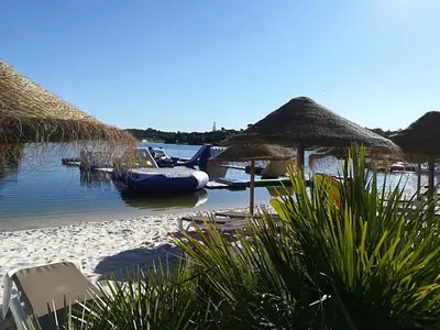 a beach with straw umbrellas and a boat in the water at Victory Village T1 & Rooftop terrace in Quinta do Lago