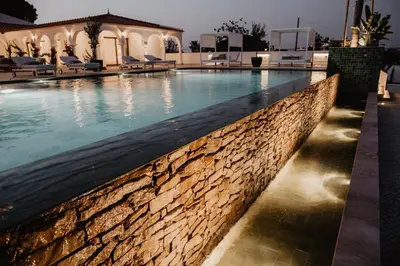 a swimming pool with a stone wall next to a building at Granvila in Quarteira