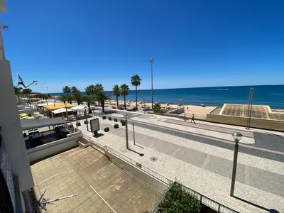 a view of a beach with palm trees and the ocean at Lusitania T2 Frente Mar em Quarteira in Quarteira