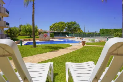 two white chairs sitting in the grass near a pool at Kamaleon Sol by Sunny Deluxe in Albufeira