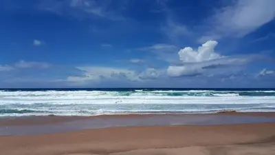 a beach with waves and a blue sky with clouds at Casa Flor de Sal - moradia no Centro de Faro! in Faro