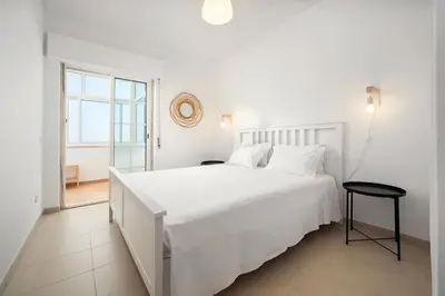 a white bedroom with a large white bed and a window at AL - Apartamento Vidal Mar in Quarteira