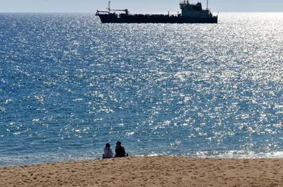 two people sitting on the beach with a ship in the water at Casa Vale Do Lobo 32 Charming 2 Bedroom Townhouse Close To Beach in Vale do Lobo