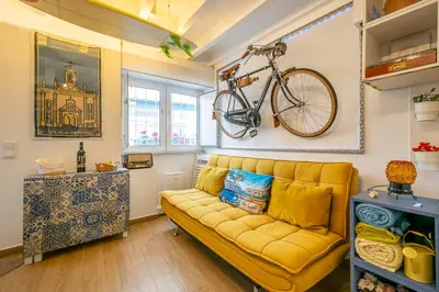 a living room with a yellow couch and a bike on the wall at Casinha da Ti Babel in Faro
