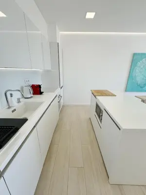 a white kitchen with white cabinets and a wooden floor at Seafront Apartment in Quarteira in Quarteira