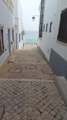 a stone walkway between buildings with the ocean in the background at Casa do Avô in Albufeira