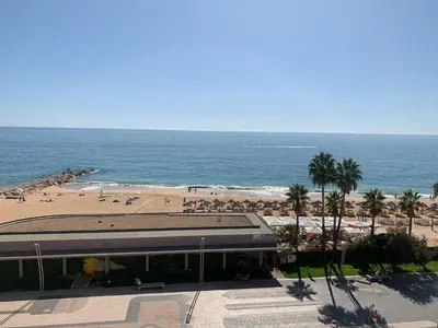 a beach with a building and a beach with people at Apartamento Frente praia in Quarteira