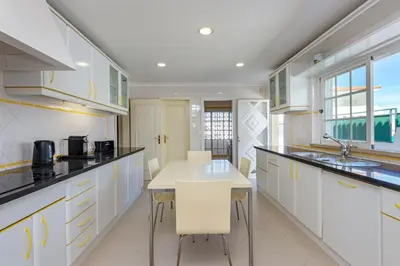 a kitchen with white cabinets and a table and chairs at Villa Cecília in Albufeira