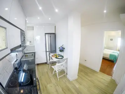 a kitchen with a table and a room with a bed at Apartamentos SweetHomes in Faro