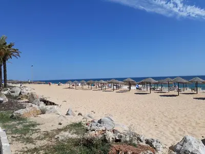 a beach with many umbrellas and rocks on it at T1 Torre 17 Vista Cidade in Quarteira