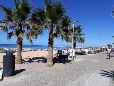 two people sitting on a bench next to the beach at T1 Mira Praia 7 - Remodelado, Ar-Condicionado, Vista Mar, Wifi in Quarteira