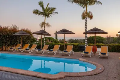 a pool with chairs and umbrellas and palm trees at Villa Florida by Algarve Vacation in Albufeira