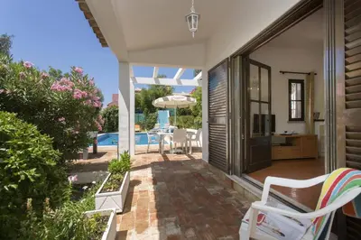 a patio with chairs and an umbrella and a pool at Villa Emilio Pequena by Villa Plus in Albufeira
