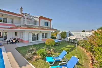 a house with a yard with chairs and an umbrella at Villa Rosa by Villa Plus in Olhos de Água