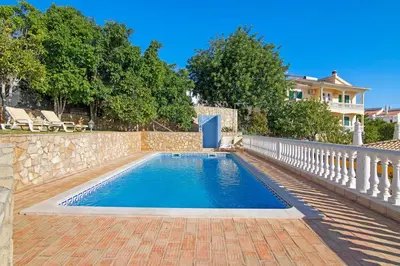 a swimming pool with a stone fence and a house at Villa Isabel in Loulé