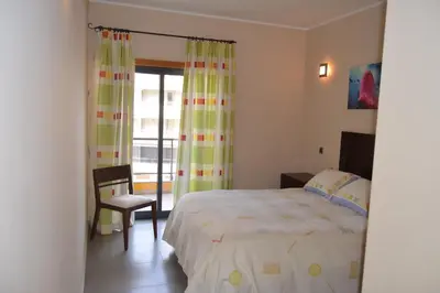 a bedroom with a bed and a chair and a window at Apartamento frente ao mar com piscina de água salgada in Quarteira